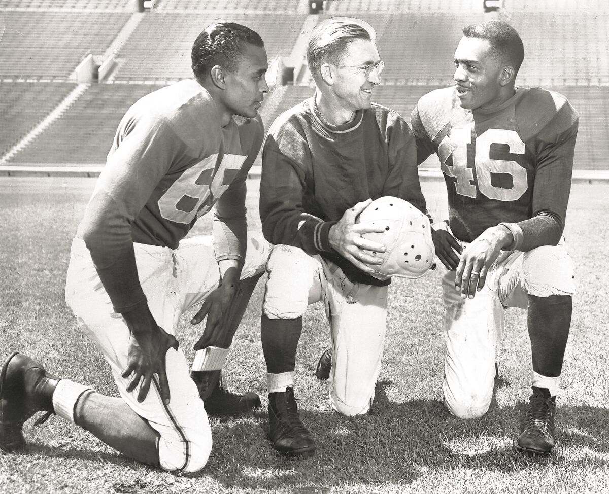 Two Black players and white coach kneel in black-and-white photo