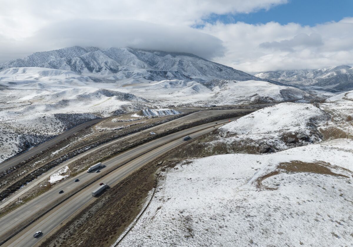 Snow covers hills and mountains on either side of a freeway.