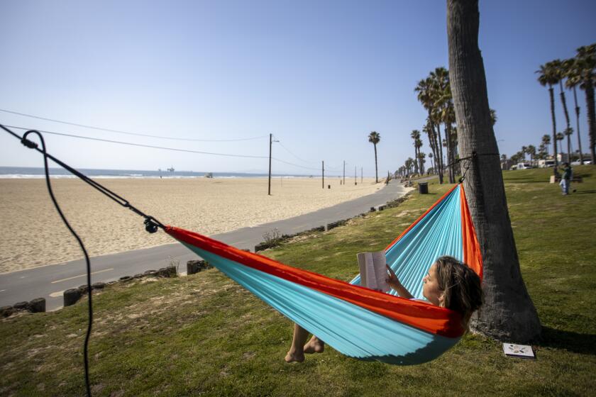HUNTINGTON BEACH, CALIF. -- THURSDAY, APRIL 2, 2020: Kylie Wortham, 18, of Huntington Beach, who was laid off when her entire company was closed due to Coronavirus social distancing rules, relaxes with a book in a hammock overlooking the beach in Huntington Beach Thursday, April 2, 2020. The pier, beach parking lots and most shops are closed due to state-mandated Coronavirus social distancing rules. The area is normally teeming with spring break visitors. (Allen J. Schaben / Los Angeles Times)