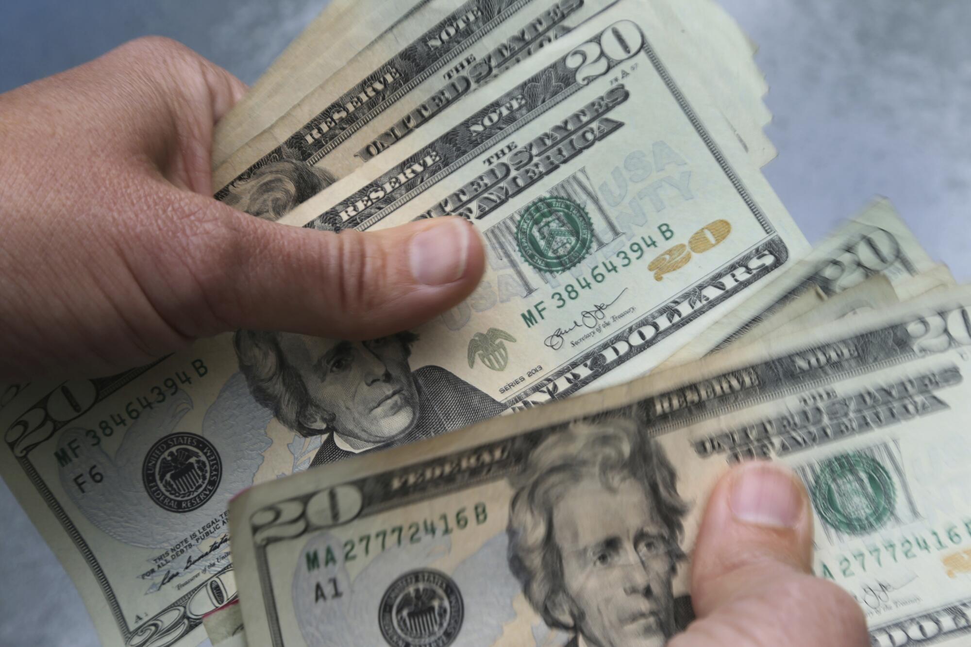 A person's hands holding $20 bills