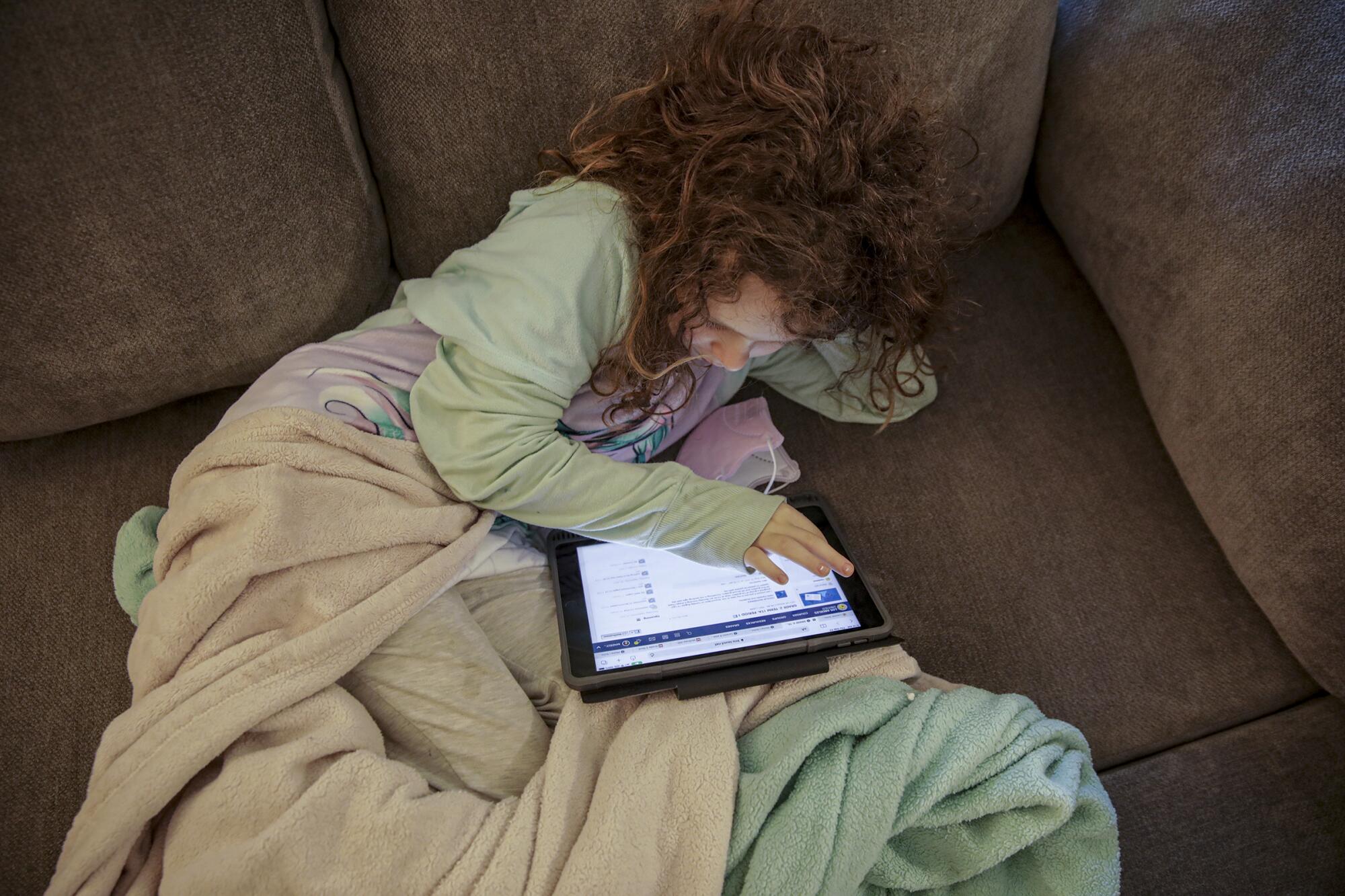Madelynn Singer, recostada en el sofá, utiliza su tableta en su casa de Porter Ranch.