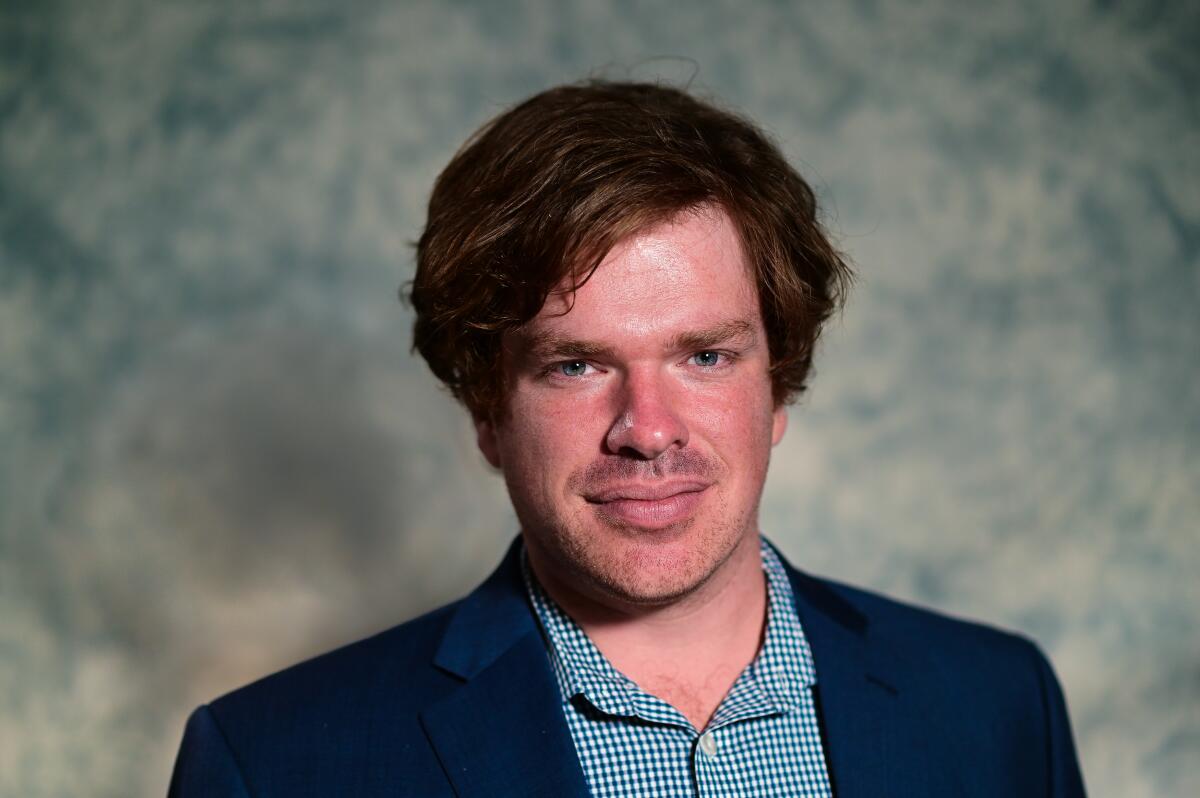 A man with flowing hair in a blue sport jacket and blue-and-white gingham shirt.