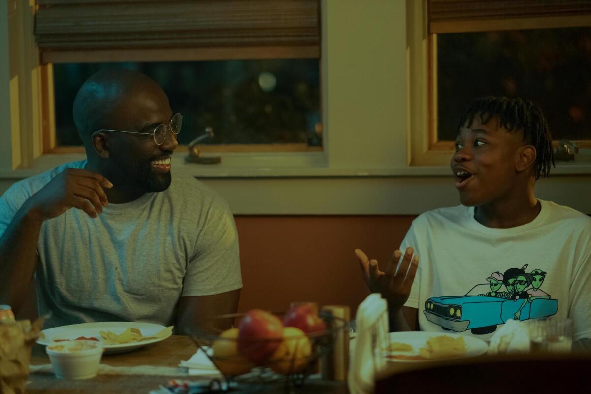 A father and a teen boy smile as they talk at a dining table.