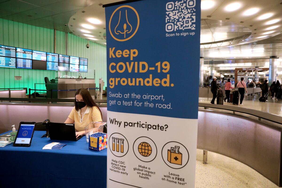 A masked person sits at a table next to a vertical "Keep COVID-19 grounded" banner.