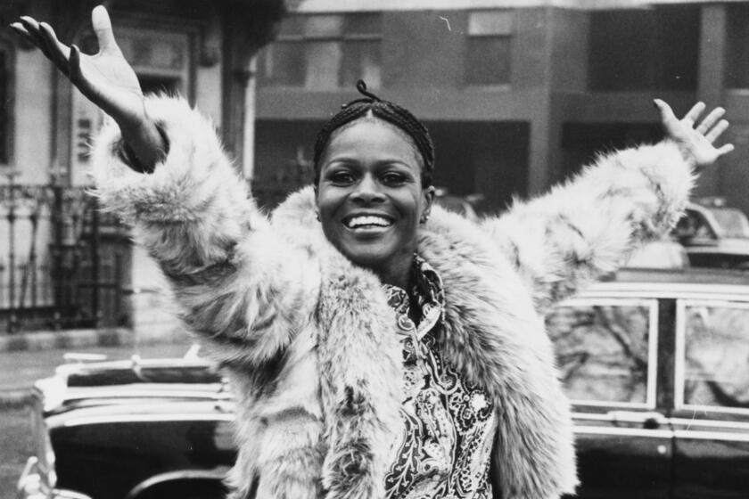 A young Cicely Tyson smiling and throwing her arms in the air while wearing a fur coat