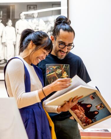 A woman and a man smile as they look through an art book that she holds