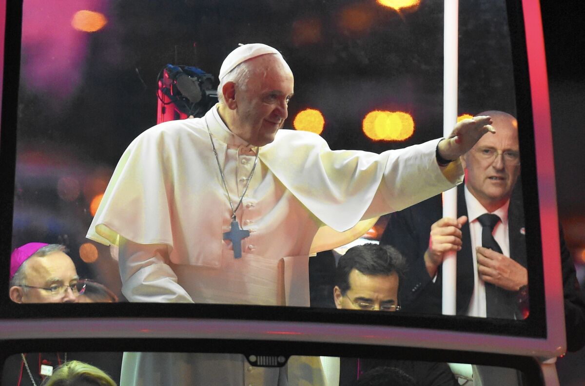 Pope Francis, standing in a vehicle, reaches a hand out to the crowd.