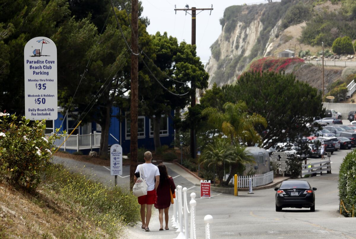 A couple who parked their car on Pacific Coast Highway walk toward Paradise Cove hoping to avoid paying the $35 daily parking fee in Malibu.