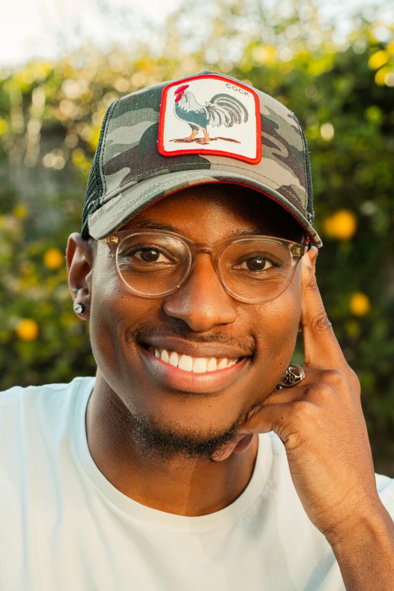 A man with glasses, a cap and a white shirt smiles at the camera.