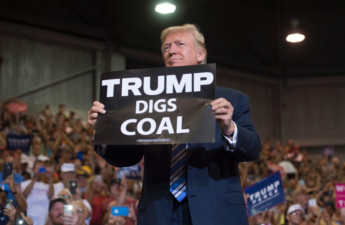 President Trump holds up a "Trump Digs Coal" sign as he arrives to speak to a West Virginia rally in August 2017. But he hasn't brought the coal industry back.
