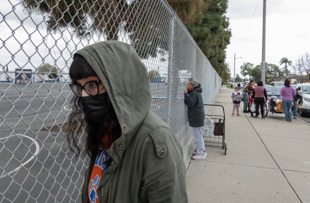 A parent in a mask waits by a school.