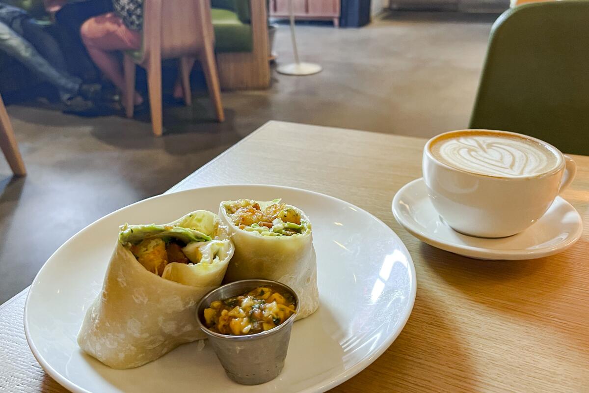 Breakfast burrito and rose latte on a wooden table.