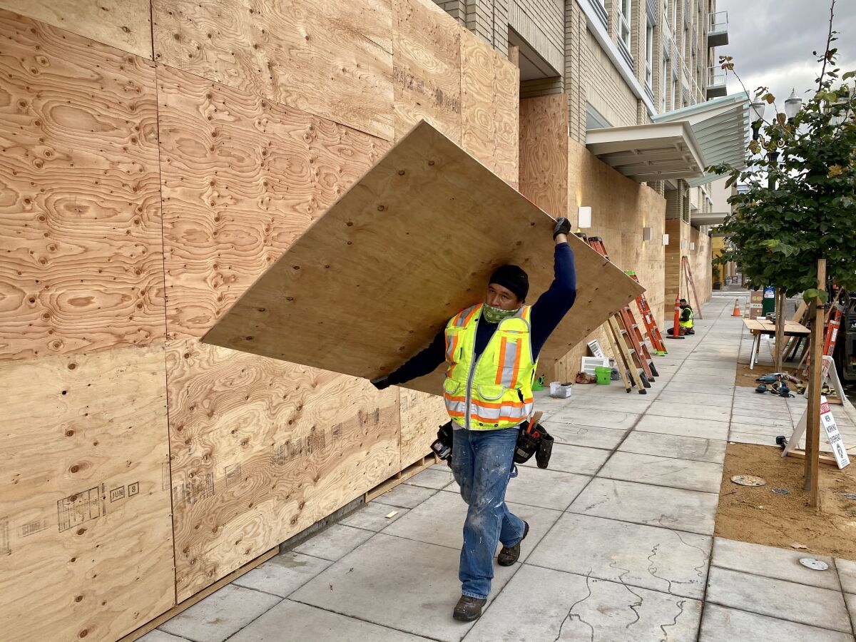 A worker carries plywood to clad the base of a Portland condominium tower Nov. 5 in case of post-election violence.