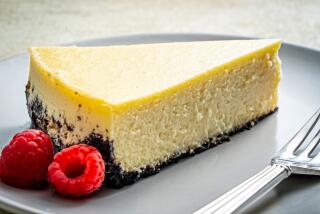 A slice of creamy cheesecake on a plate with raspberries garnishing it.