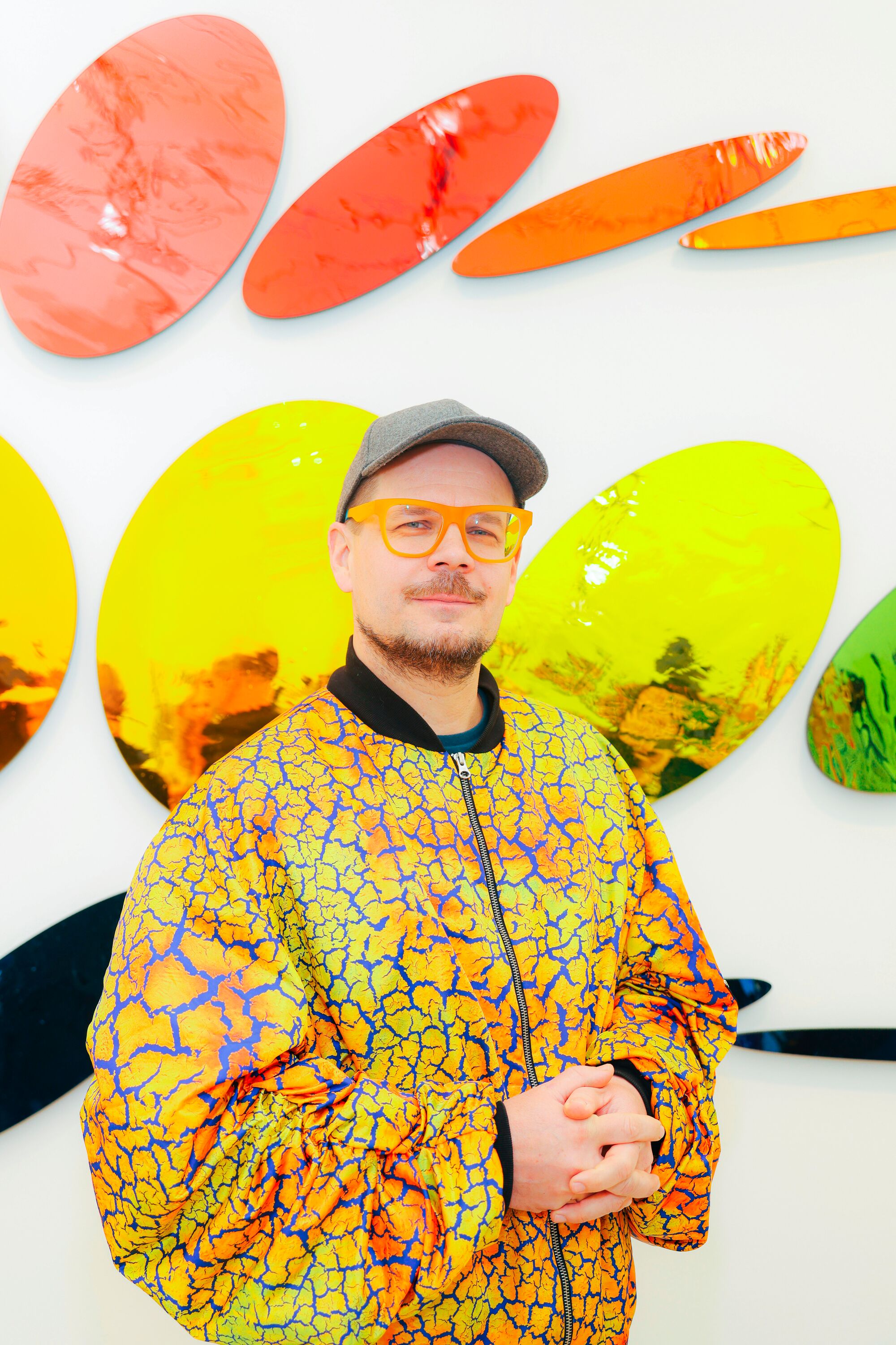 A person in a colorful yellow jacket poses in front of a piece of art.