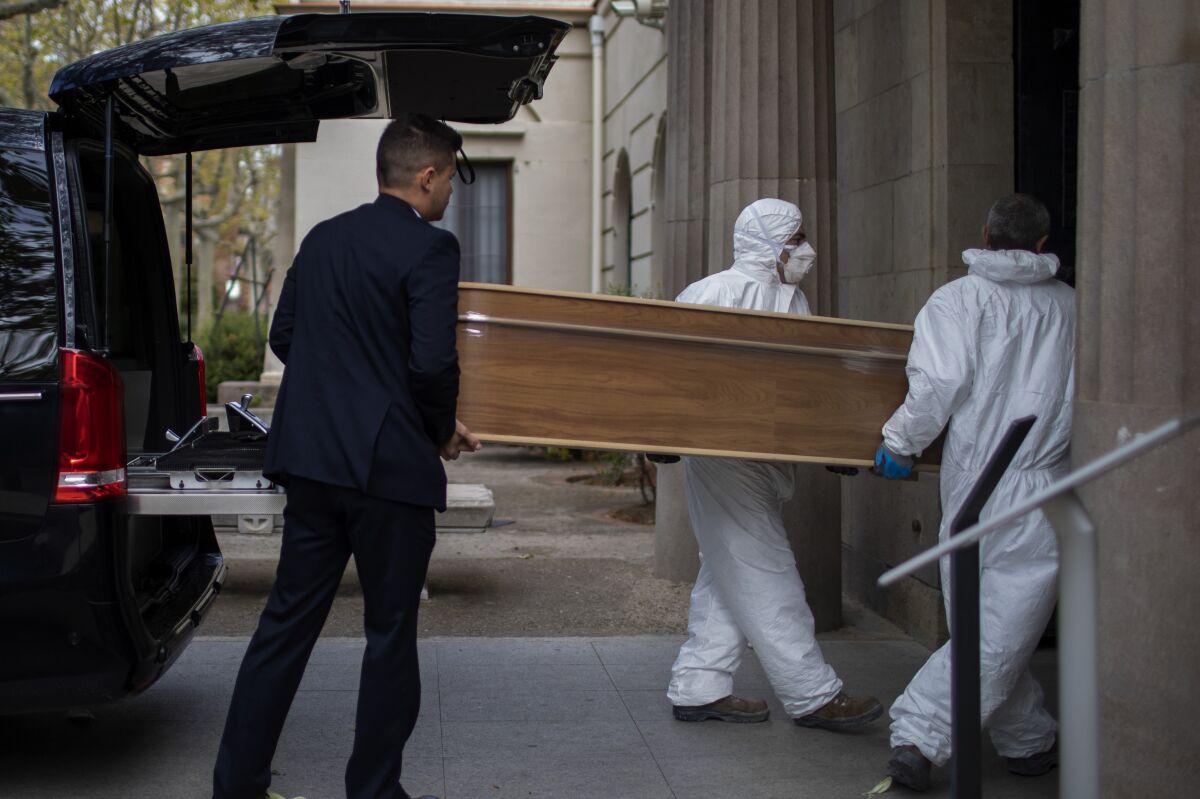 Empleados de una funeraria trasladan un ataúd para un entierro en un cementerio en Barcelona durante el brote del coronavirus en España, el viernes 27 de marzo de 2020. (AP Foto/Emilio Morenatti)