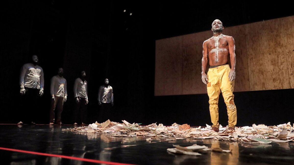 Dancer Jean Kumbonyeki Deba stands among the papers representing the work of Congolese writer Kobako, who is one of the people commemorated in Faustin Linyekula's "In Search of Dinozord" at REDCAT.