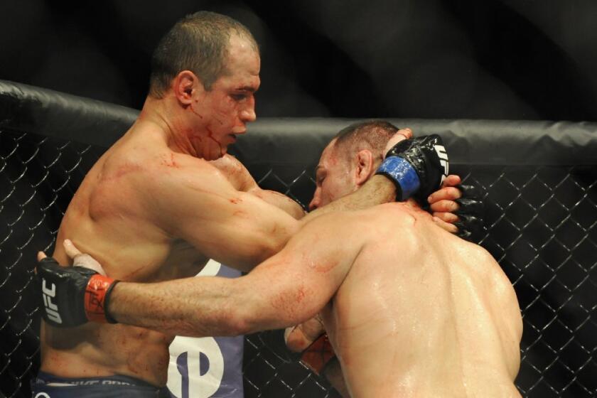 A bloodied Junior Dos Santos, left, tries to hold off Cain Velasquez.