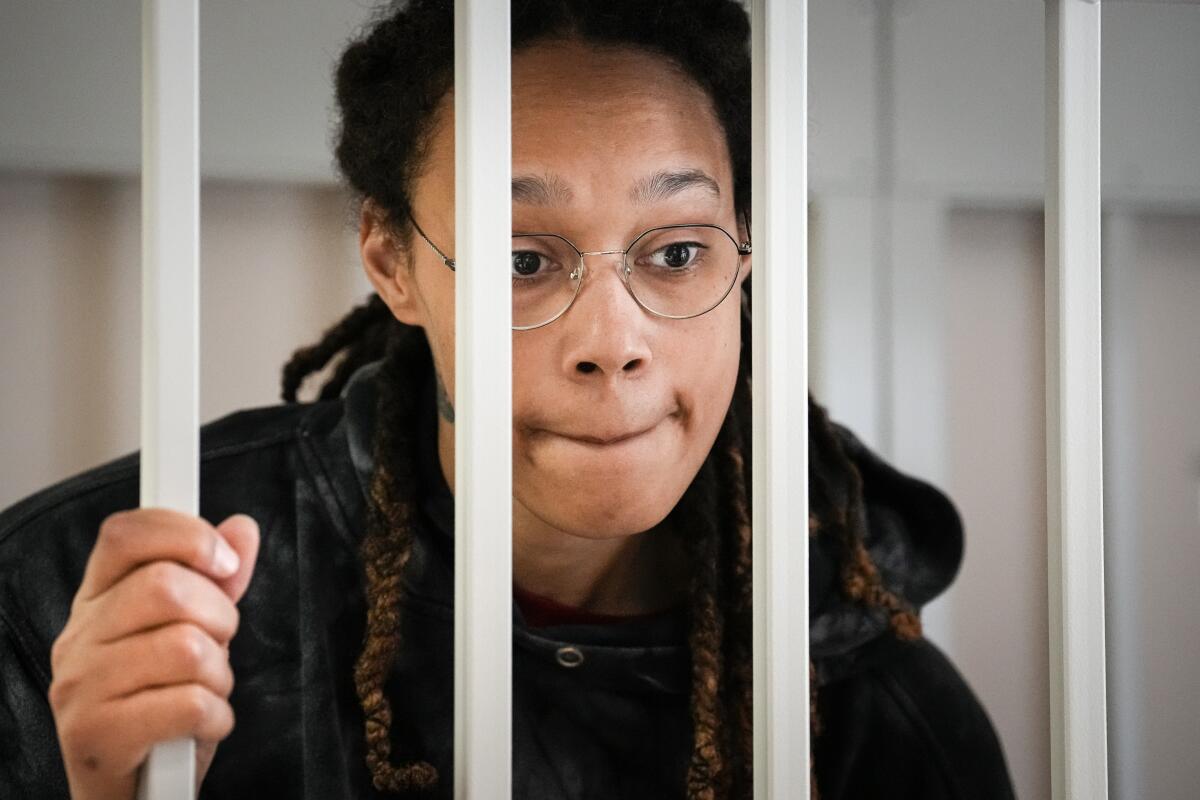 WNBA star Brittney Griner speaks to her lawyers while standing in a cage in a courtroom.