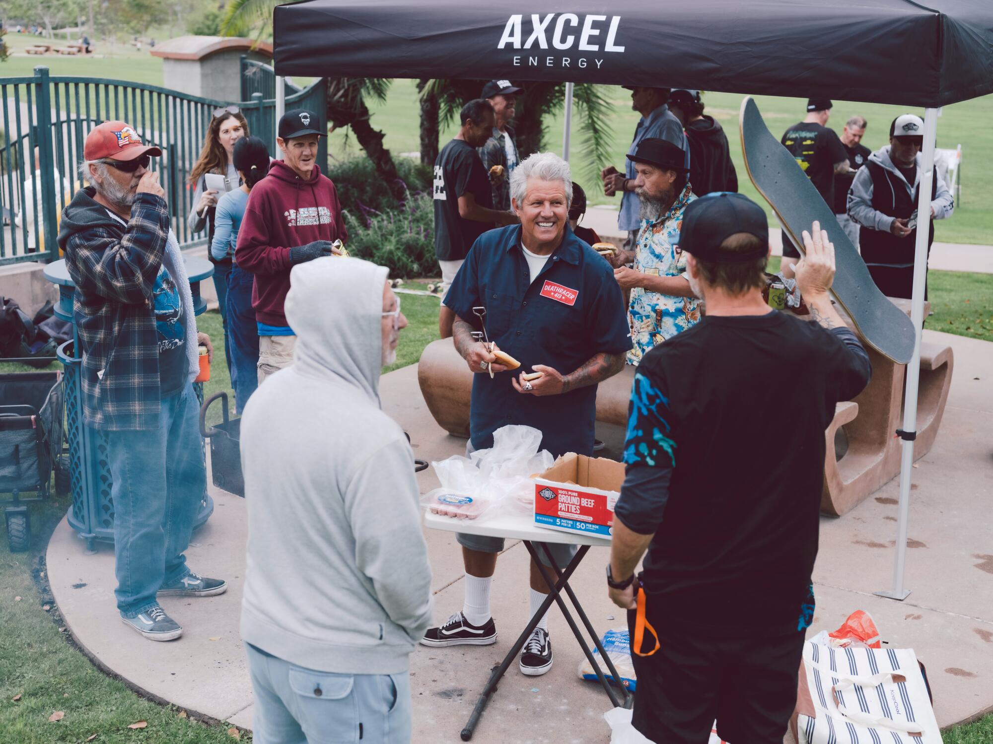 Men gather around the grill as a barbecue is underway.