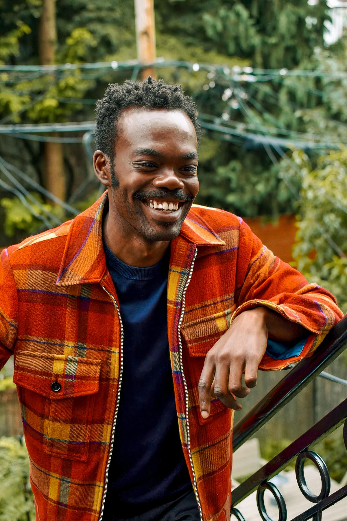 William Jackson Harper in an orange and yellow plaid jacket in a backyard