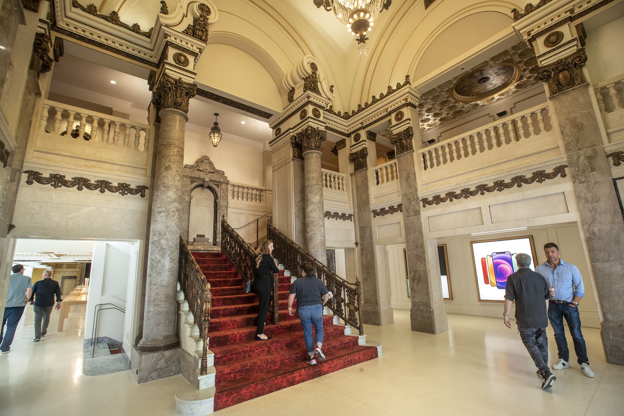 Customers ascend a staircase clad in red carpet that is framed by brass handrails and marble columns