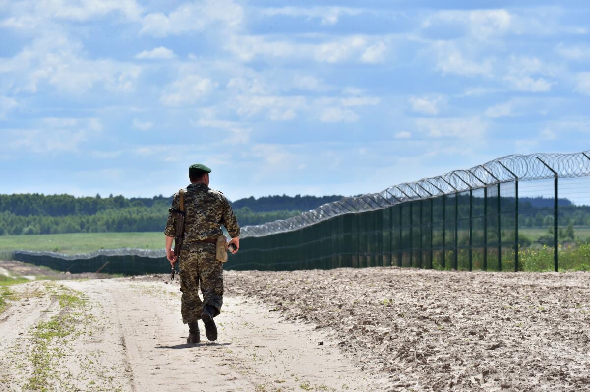A border guard walks on a road along a tall fence topped with barbed wire 