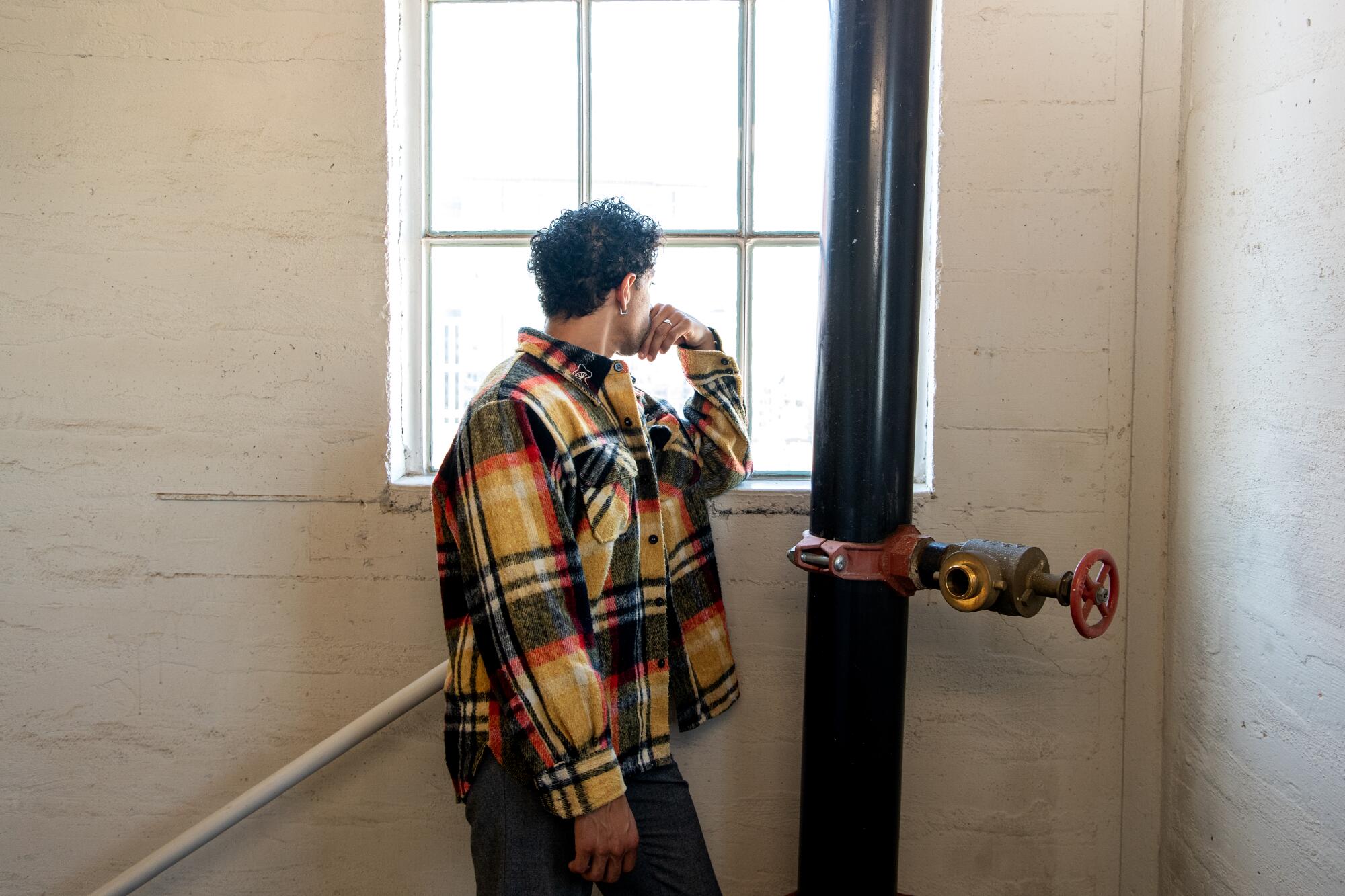 A man stands in a stairwell wearing a plaid yellow, green, and red jacket.