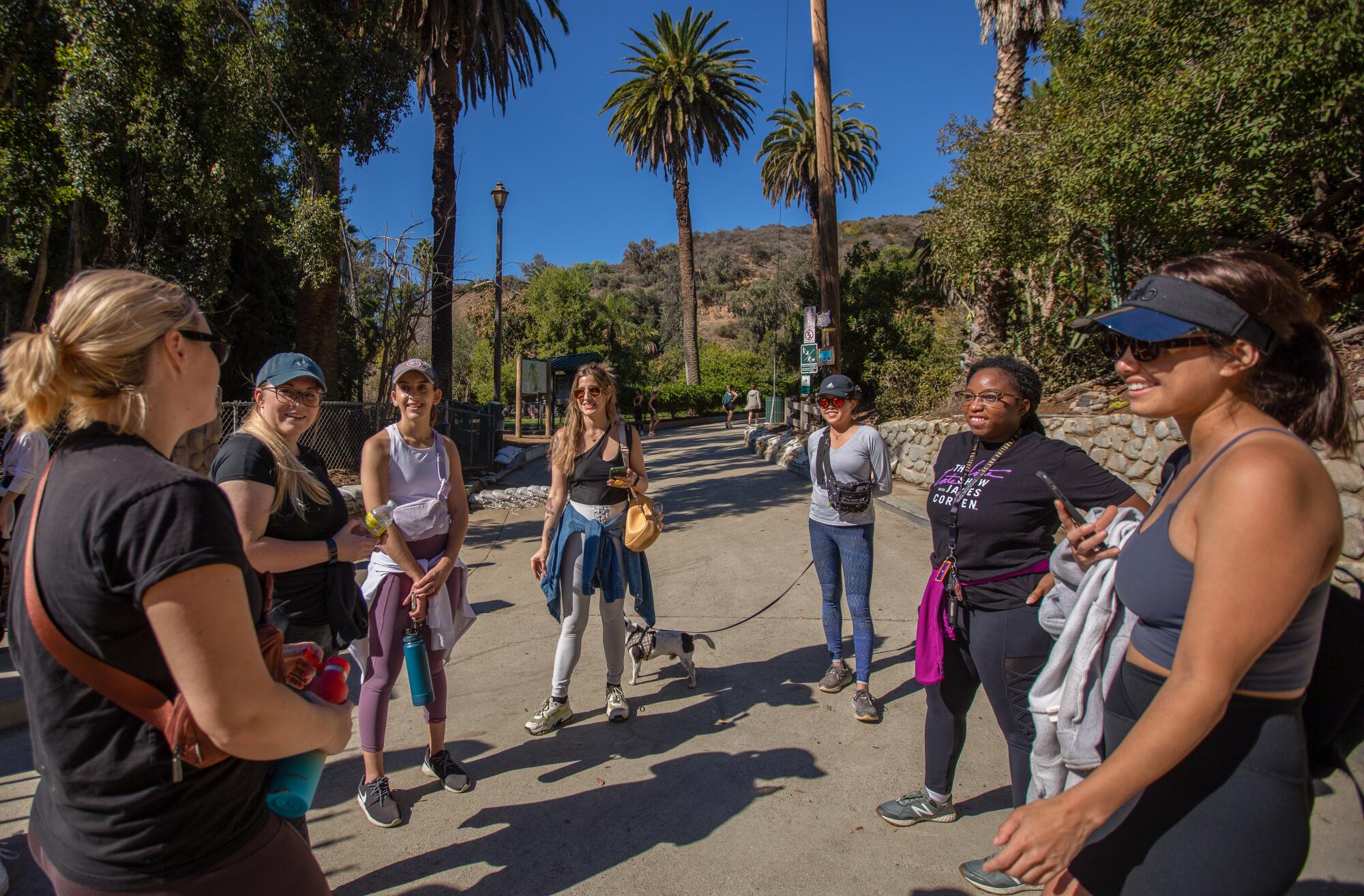 A group of women standing in a circle at the mouth of a trailhead in a park.