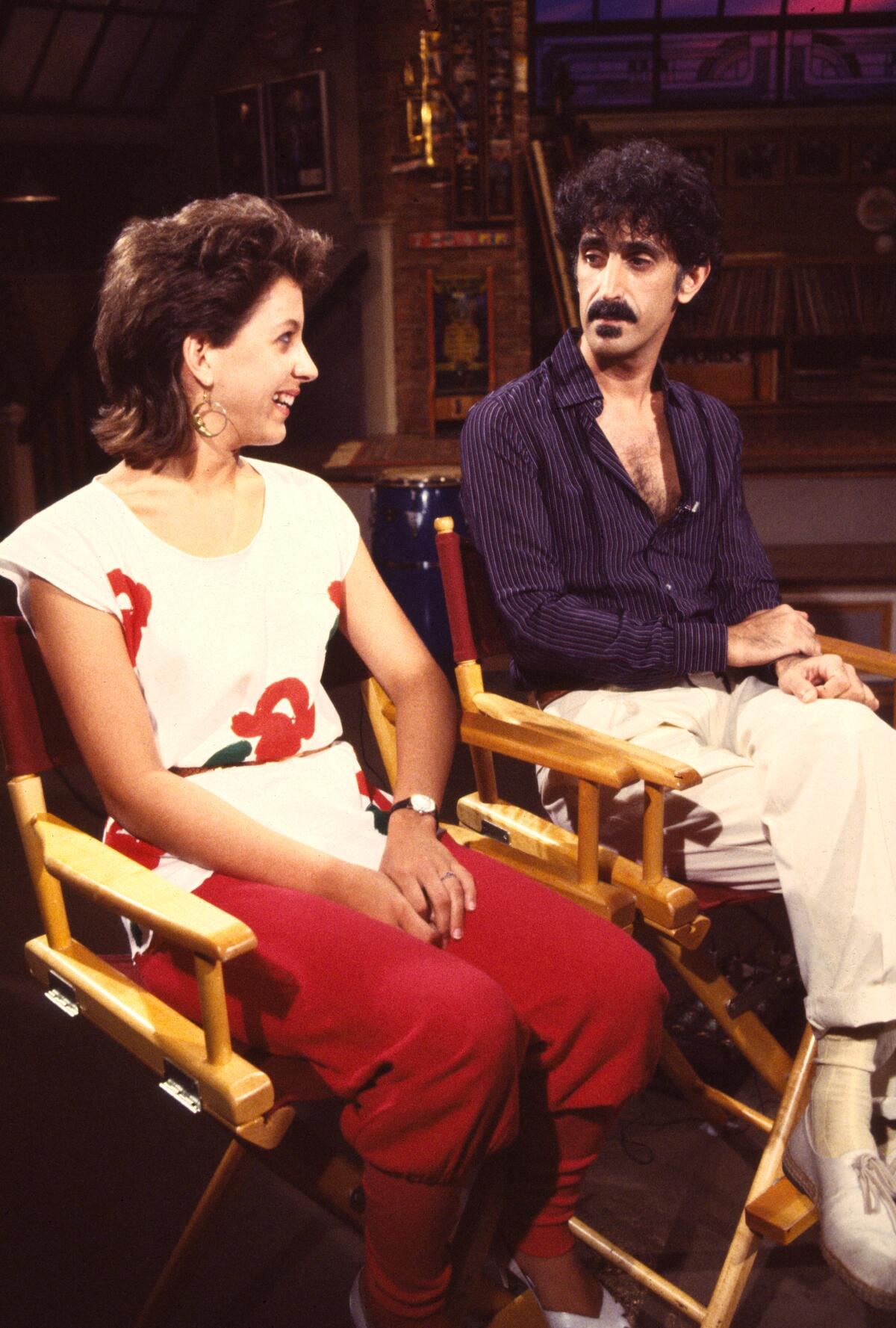 Moon Unit Zappa smiles at her father, Frank Zappa, as they sit in director's chairs.