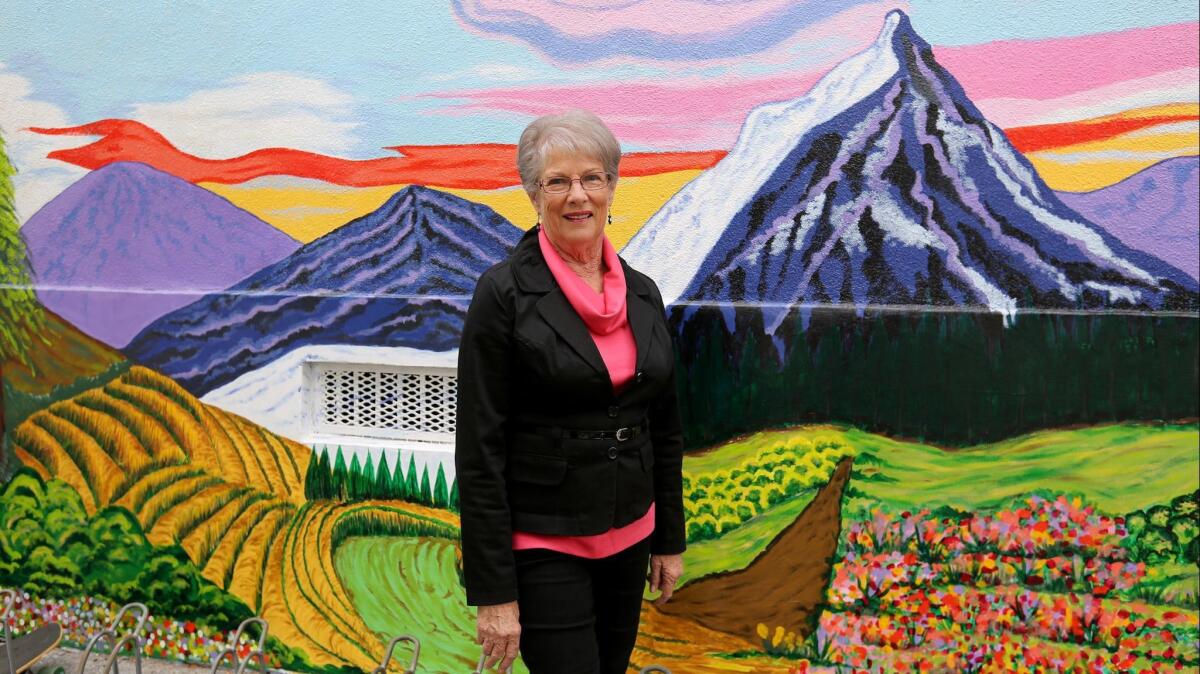 Muralist and former teacher Helene Cob stands next to part of a mural she designed, depicting scenes from San Francisco and mountains, at Edison Elementary.