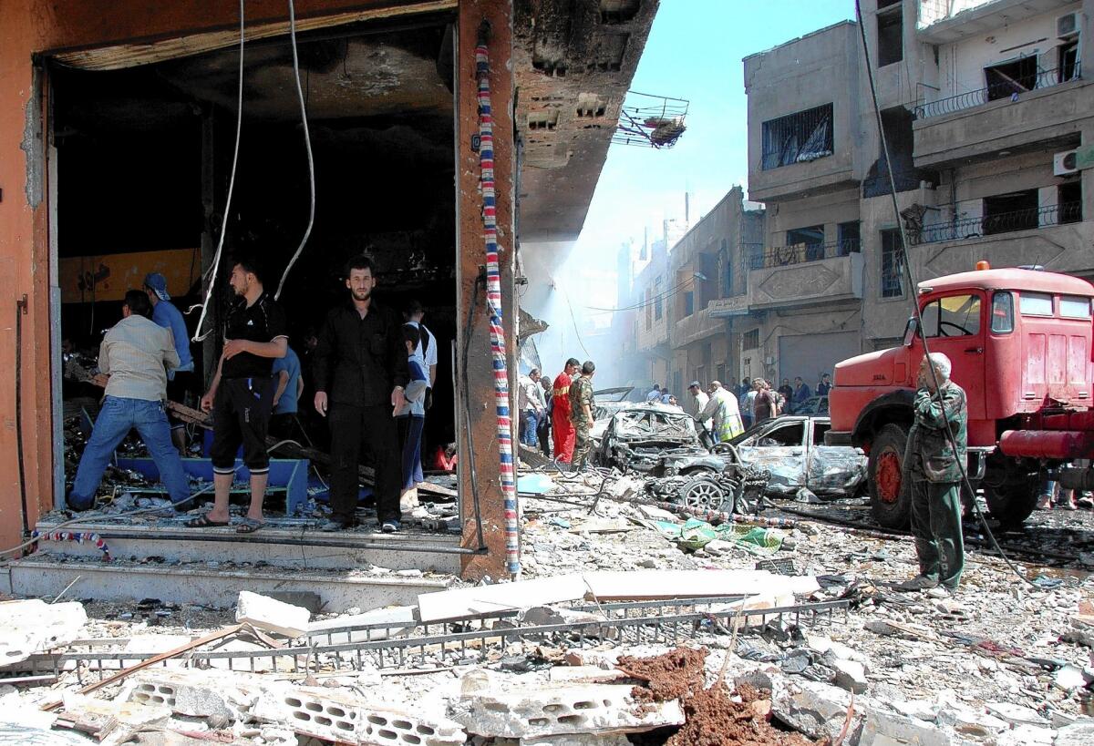 Civilians and emergency personnel survey the site of a car bombing in the Syrian city of Homs.