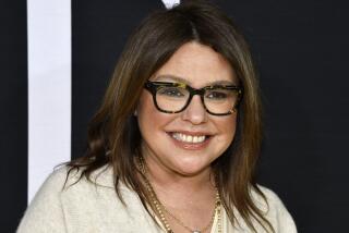 Rachael Ray in thick black glasses and a white tunic 
