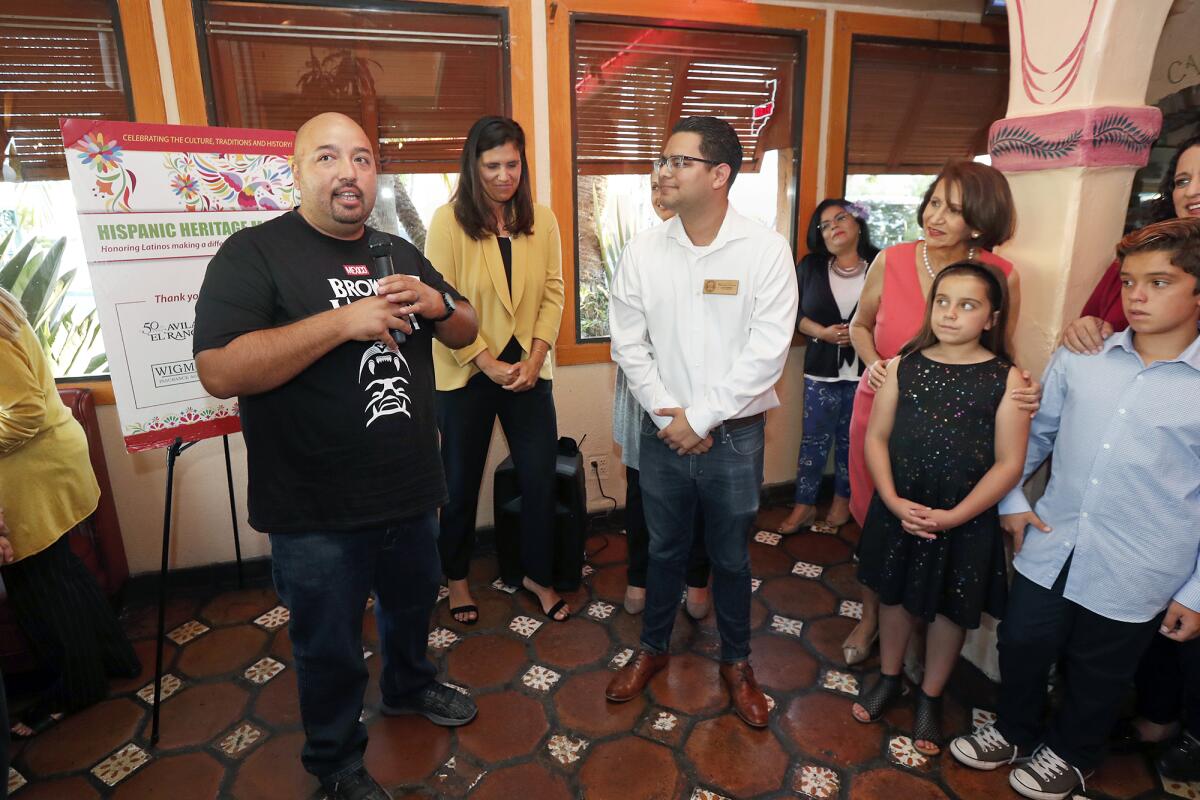 Andy Godinez, 37, left, a lifelong Costa Mesa resident and an employee in the city’s code enforcement division, speaks Wednesday after being recognized by Councilman Manuel Chavez, center, for his contributions to the community during a celebration of National Hispanic Heritage Month at Avila’s El Ranchito in Costa Mesa.