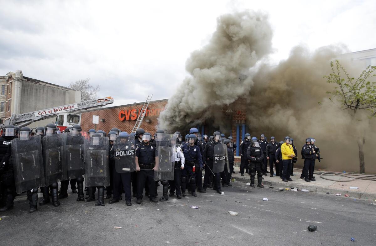 Police stand in front of a burning store on April 27, 2015, during unrest following the funeral of Freddie Gray in Baltimore. Gray died from spinal injuries about a week after he was arrested and transported in a Baltimore Police Department van.