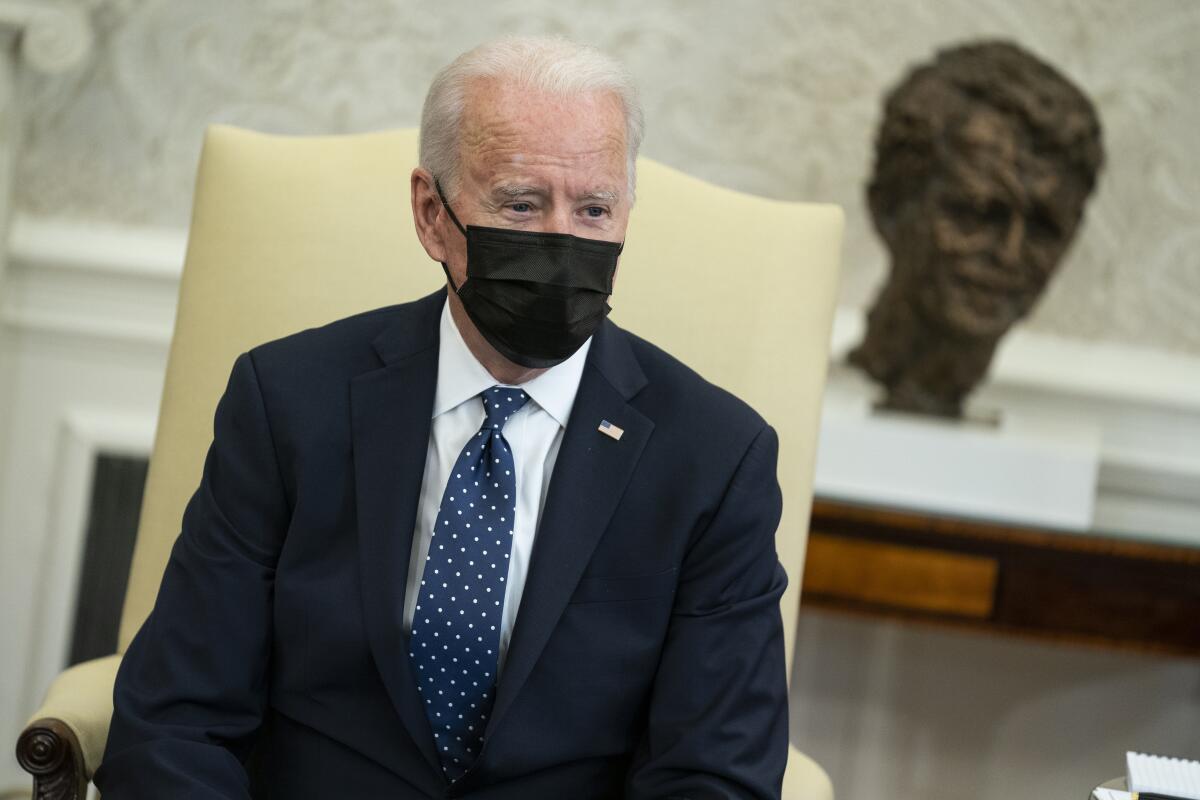 A mask-wearing President Biden speaks during a meeting at the White House.