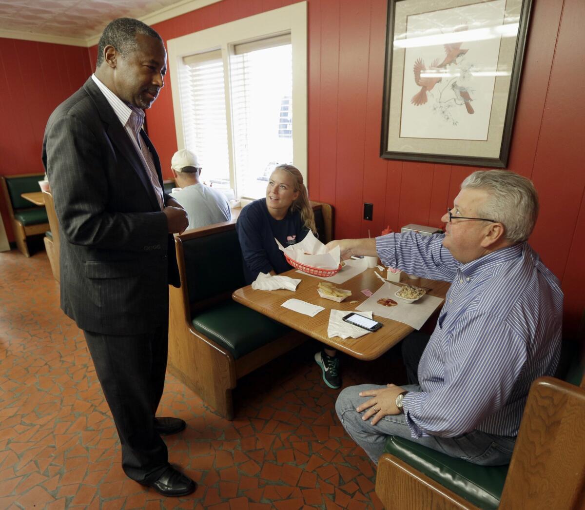 Republican presidential candidate Ben Carson, left, is offered a hushpuppy by diners Rex Savage and his daughter Nicole on a campaign stop in Lexington, N.C.