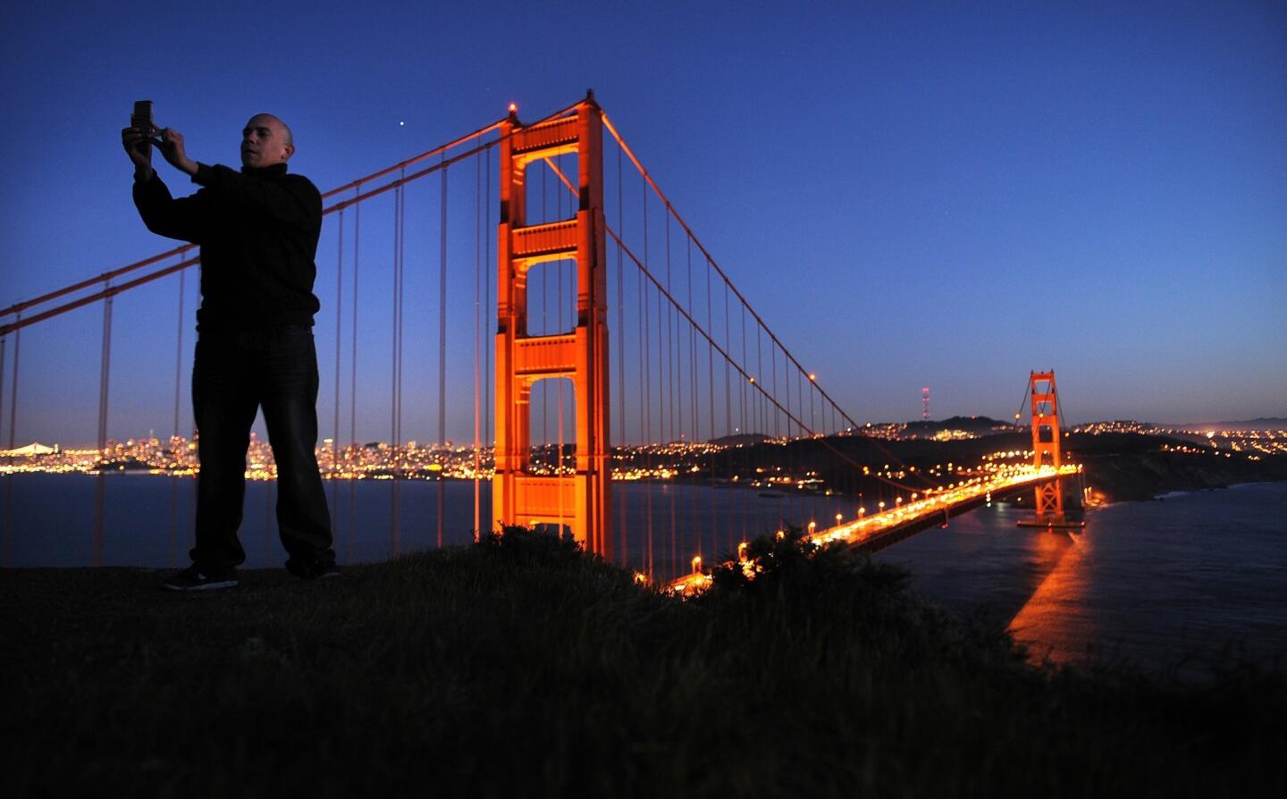 Carlos Rodriquez takes a photo of himself and the Golden Gate Bridge at dusk.