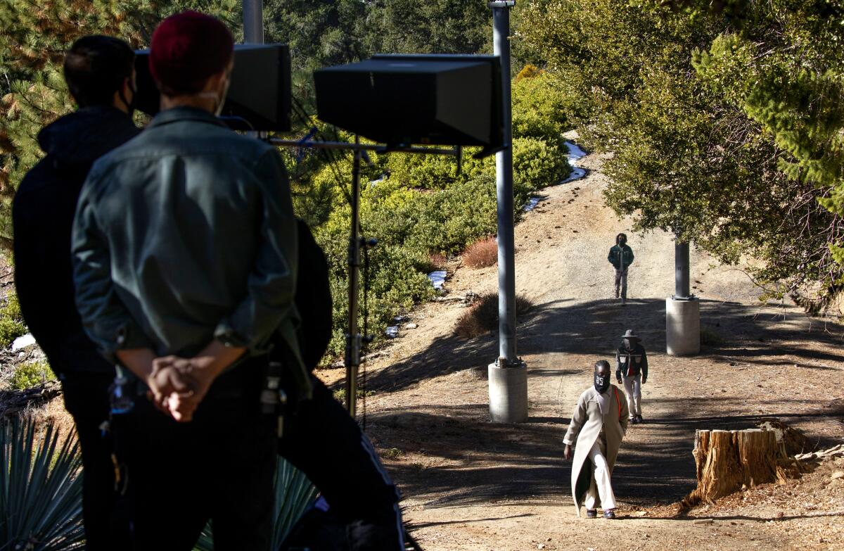 A camera crew watches models walk through a forest.