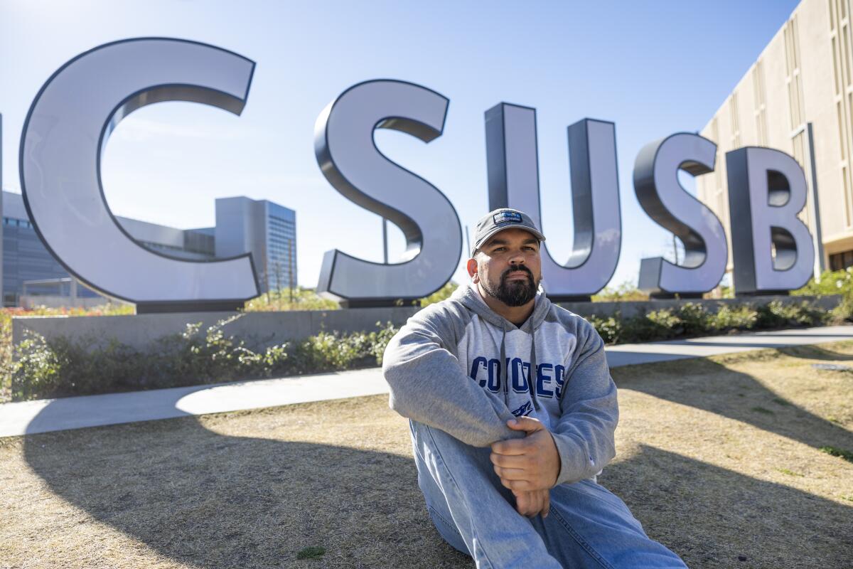 Michael Griggs sits in front of a CSUSB sign. 