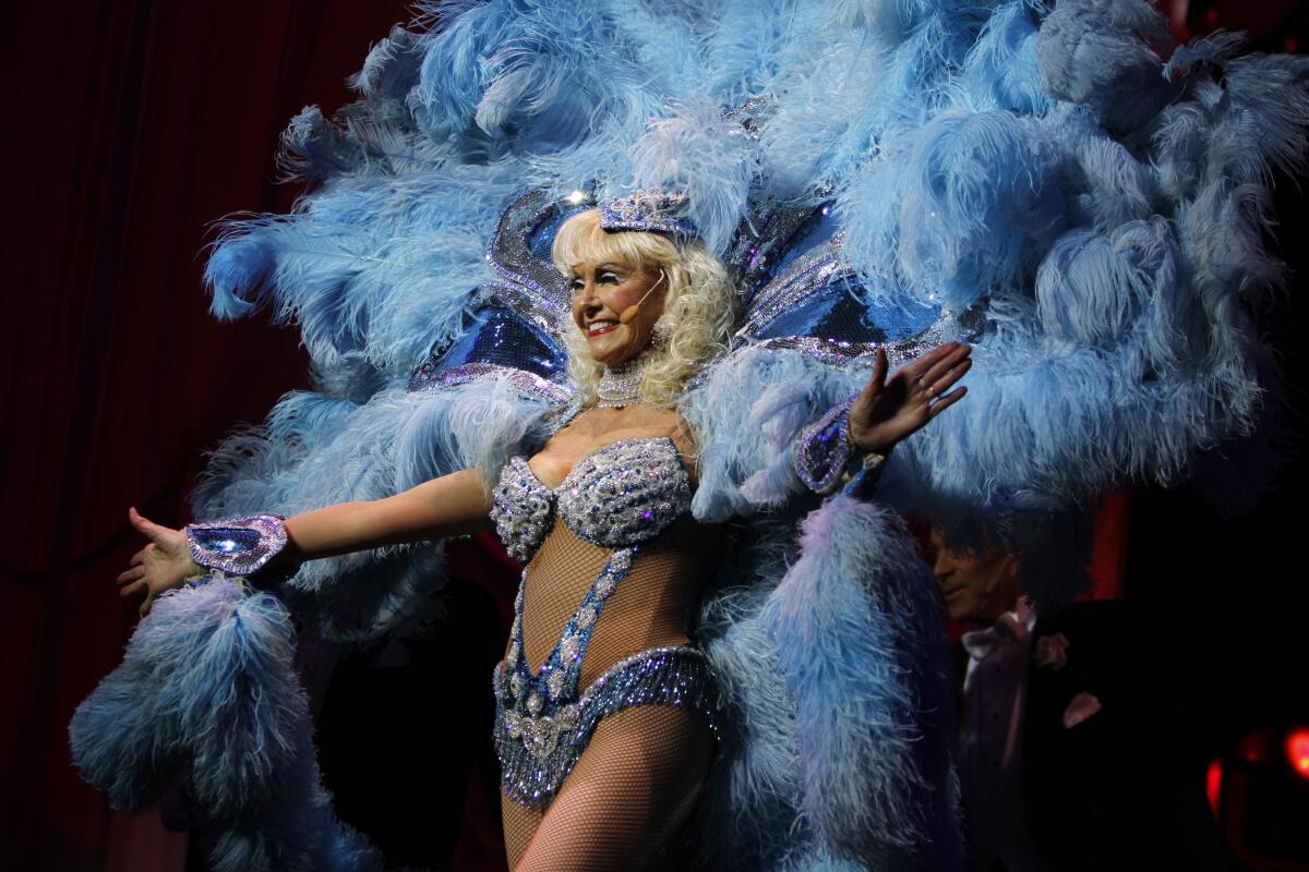 A 77-year-old blond woman in a blue feathery showgirl costume.