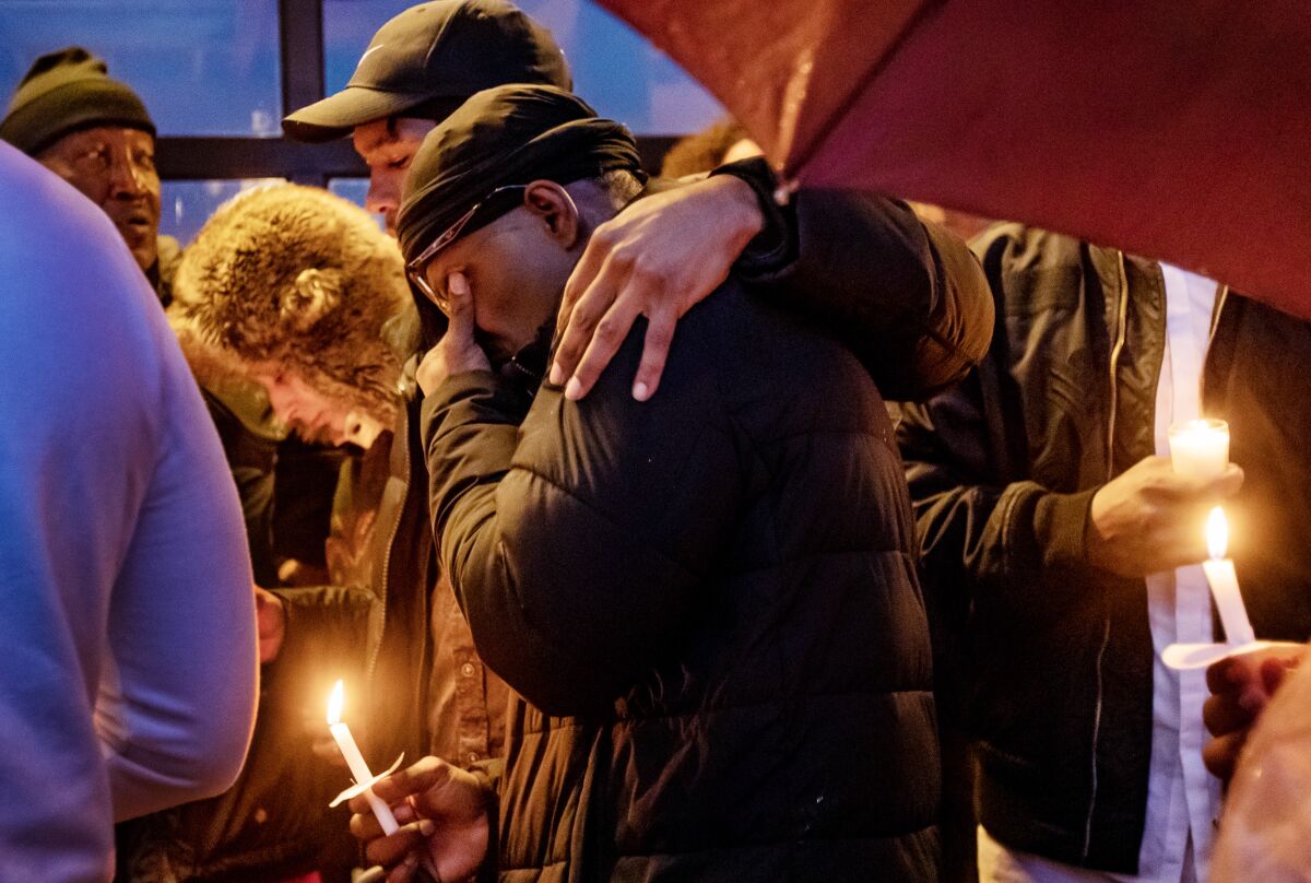 People hold candles and embrace at a vigil.
