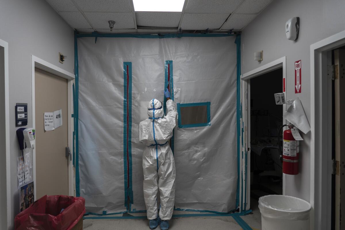 A medical staff member in a white protective suit zips closed the barrier on a COVID-19 intensive care unit 