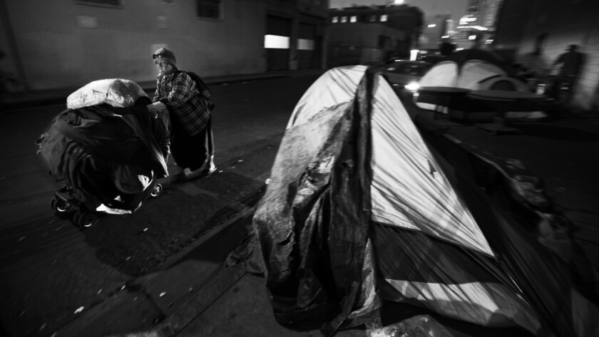 At dawn, a homeless woman pushes her cart down Winston Street near skid row in downtown Los Angeles.
