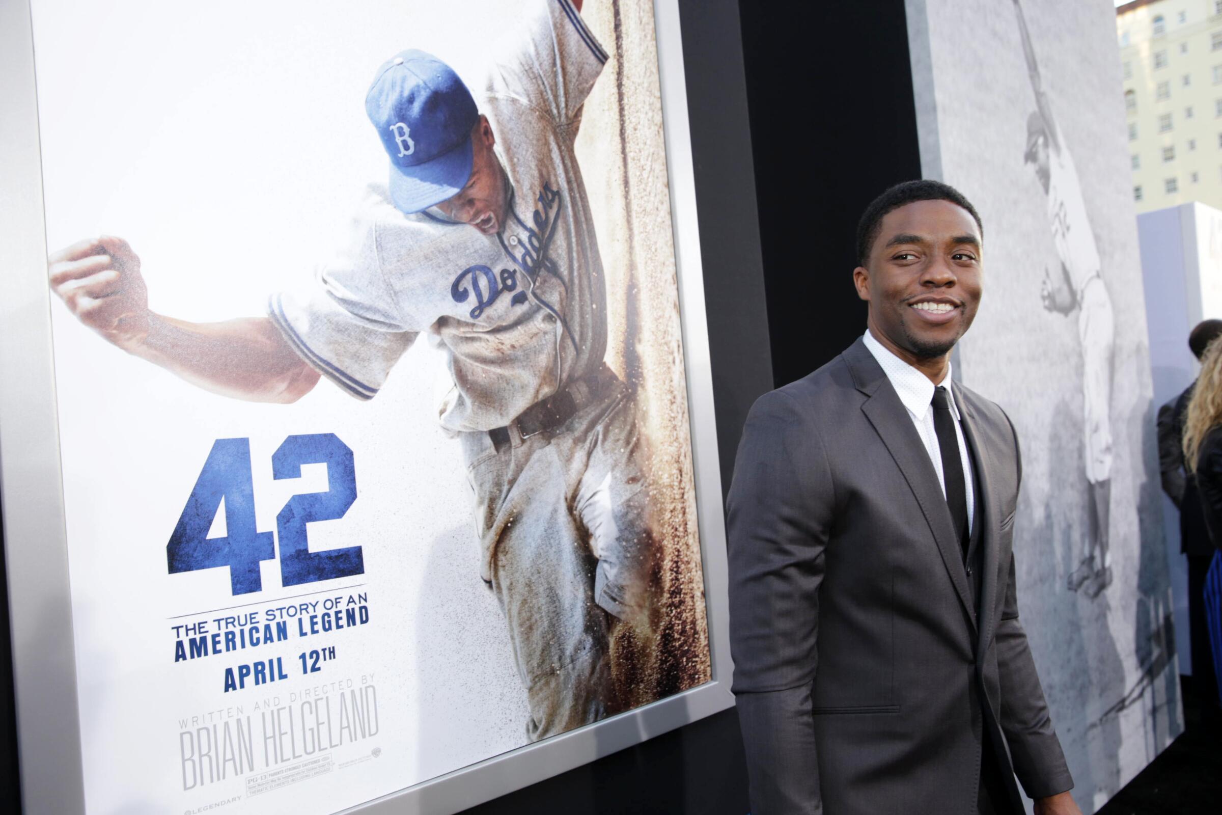 Chadwick Boseman stands on a red carpet in front of a "42" movie poster. 