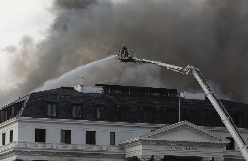 Firefighters, atop a hoist, fight the re-ignited fire at Parliament in Cape Town, South Africa, Monday, Jan 3, 2022. Firefighters are again on the scene after a major blaze tore through the precinct a day earlier. (AP Photo/Nardus Engelbrecht)