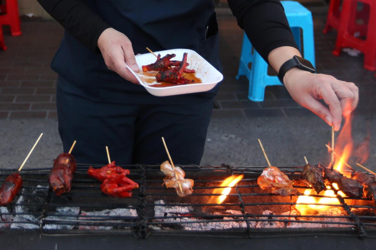 LOS ANGELES, CA - JANUARY 14, 2022 - - Angel Napiere uses one of the communal grills to cook skewers of meat at Dollar Hits restaurant along Temple Street in Historic Filipinotown in Los Angeles on January 14, 2022. (Genaro Molina / Los Angeles Times)