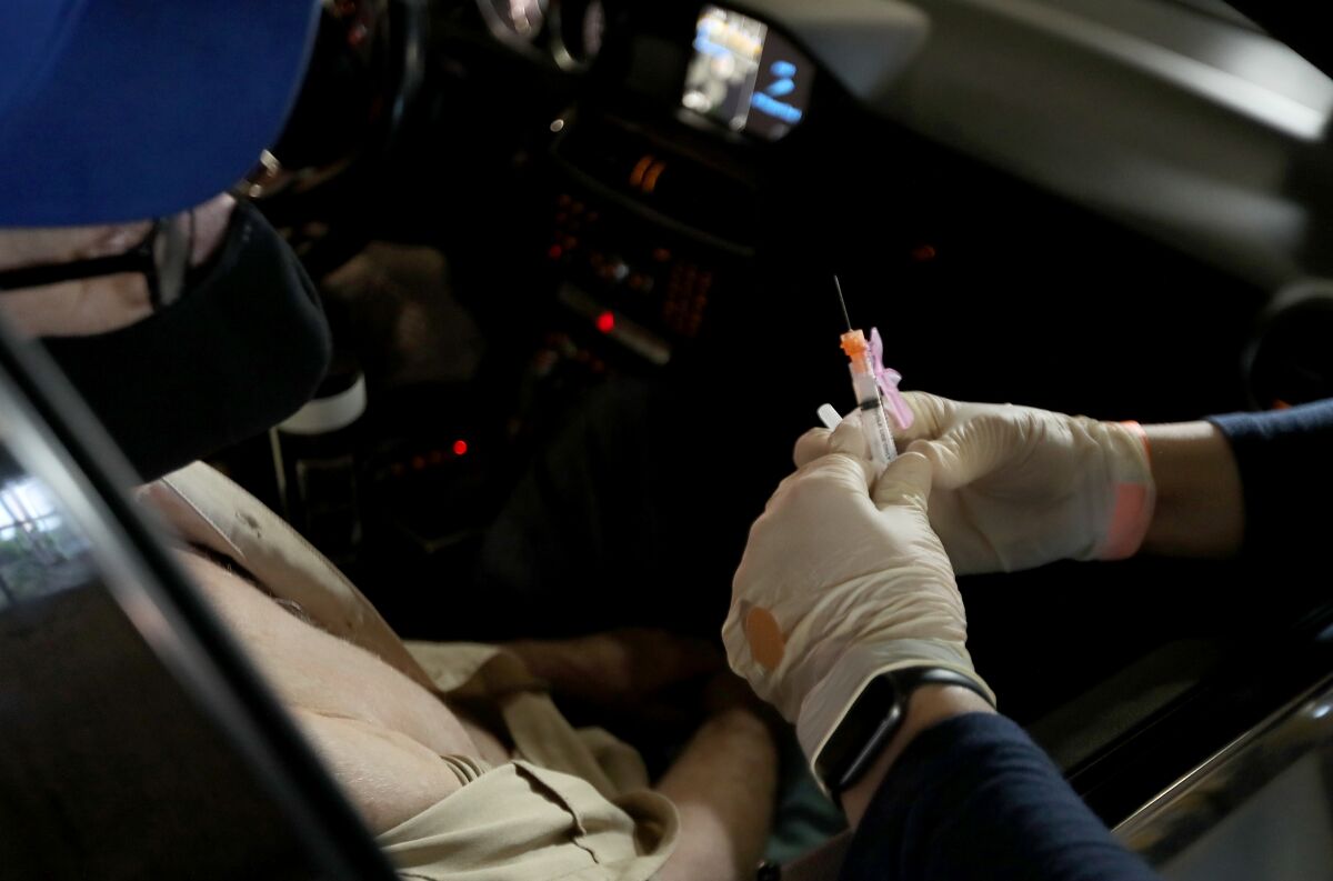 A doctor holds a COVID-19 vaccine before injecting a person in a car.