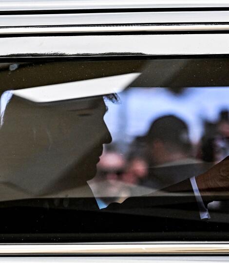 Former President Trump seen in silhouette inside a car, whose window reflects people outside