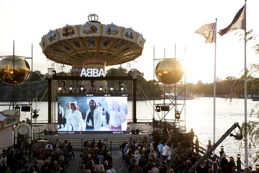 At water's edge in Stockholm, an audience watches a big screen announcing ABBA's return